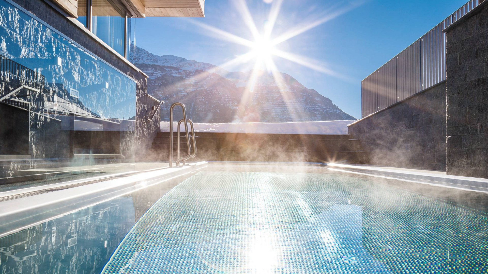 Dampfender Außenpool mit Sonnenlicht und Bergkulisse