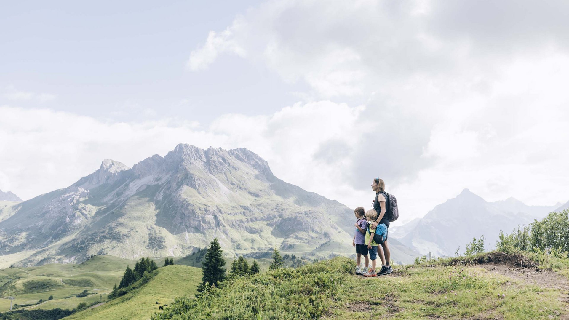 Frau mit zwei Kindern beim Wandern in den Bergen mit Blick auf Gipfel